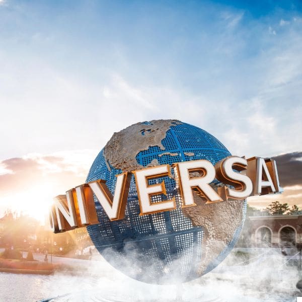 a large globe with the word "universal" in bold letters encircling it, set against a clear blue sky. the globe features map outlines, and light mist surrounds its base. sunlight creates a warm glow, suggesting a sunrise or sunset.