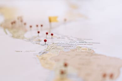 a map with red pins marking various locations across central and south america, with a yellow flag pin prominently placed. the map and pins are slightly out of focus, creating a soft, blurred effect.