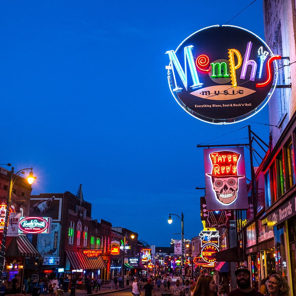 destination memphis 3 a lively street scene in memphis at dusk with vibrant neon signs for clubs and restaurants. crowds of people walk along the street, and colorful lights illuminate the buildings. the sky is a deep blue, enhancing the lively atmosphere.