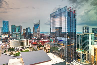 a cityscape of nashville, tennessee, emerges as a prime destination, featuring modern skyscrapers and iconic buildings with reflective glass surfaces. the cloudy sky looms over the urban skyline, highlighting the contrast between architecture and nature.
