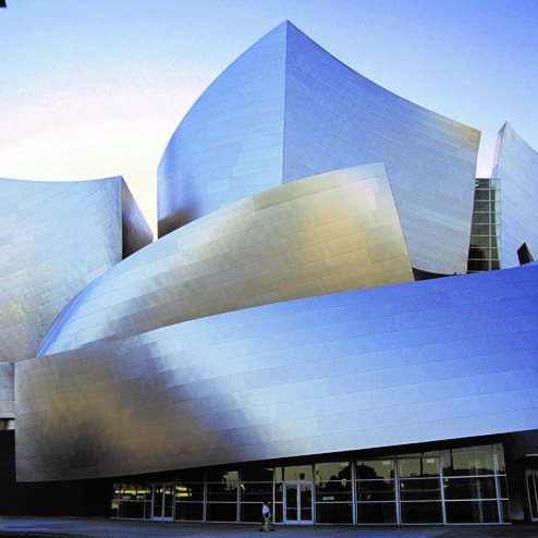 destination los angeles & southern california 7 a modern building with curved, metallic surfaces reflecting light in various shades of silver and blue against a clear sky. the structure features dynamic, sculptural forms and large glass panels at street level.