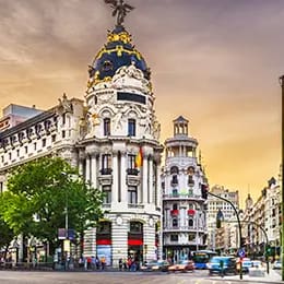 a picturesque cityscape featuring a grand, ornately decorated building with a domed roof and statues, set against a colorful sunset sky. the street below is bustling with cars and people, lined by additional historic architecture. a picturesque cityscape featuring a grand, ornately decorated building with a domed roof and statues, set against a colorful sunset sky. the street below is bustling with cars and people, lined by additional historic architecture.