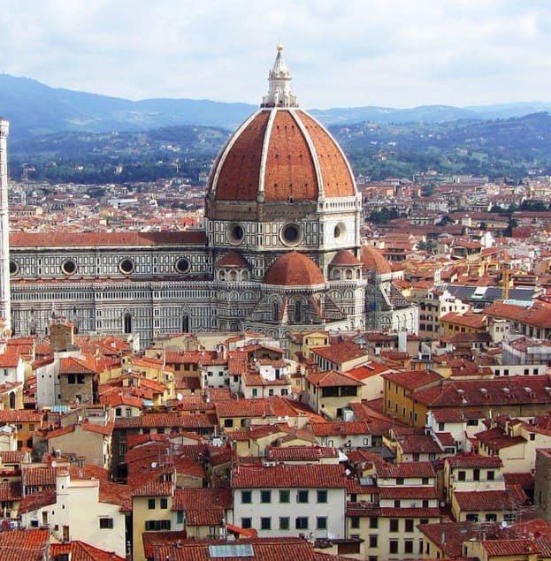 destination italy 3 aerial view of florence, italy, showcasing the red-tiled rooftops and the prominent florence cathedral with its large dome. the surrounding tuscan hills are visible in the background under a partly cloudy sky.